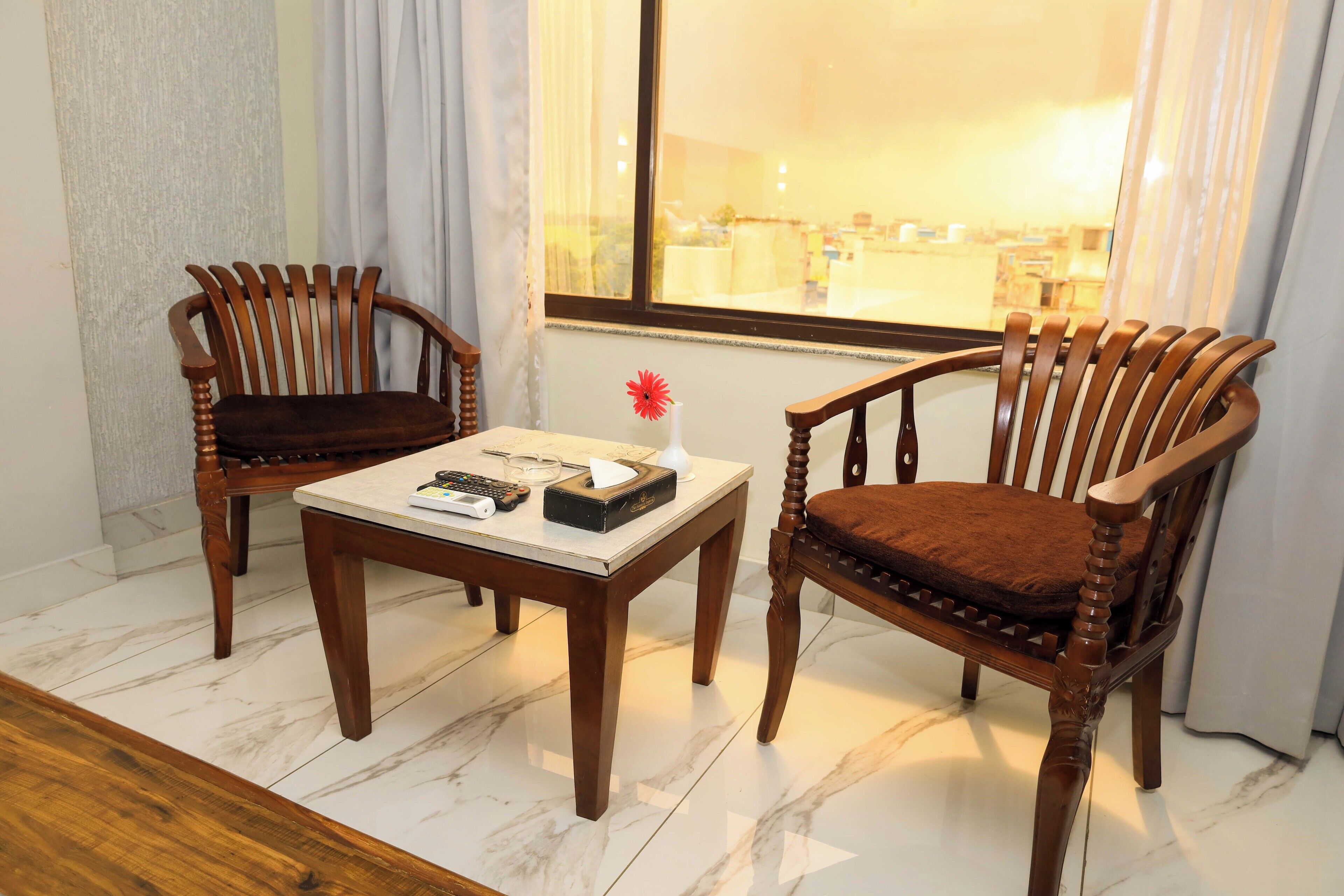A room with two wooden chairs and a table, a vase with a flower, and a window with a view of the outside.