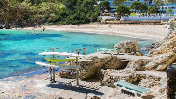 A beach with clear turquoise water, rocky shore, and lounge chairs.
