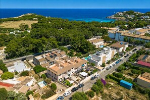 An aerial view of a coastal residential area with houses, a road, and a view of the sea.