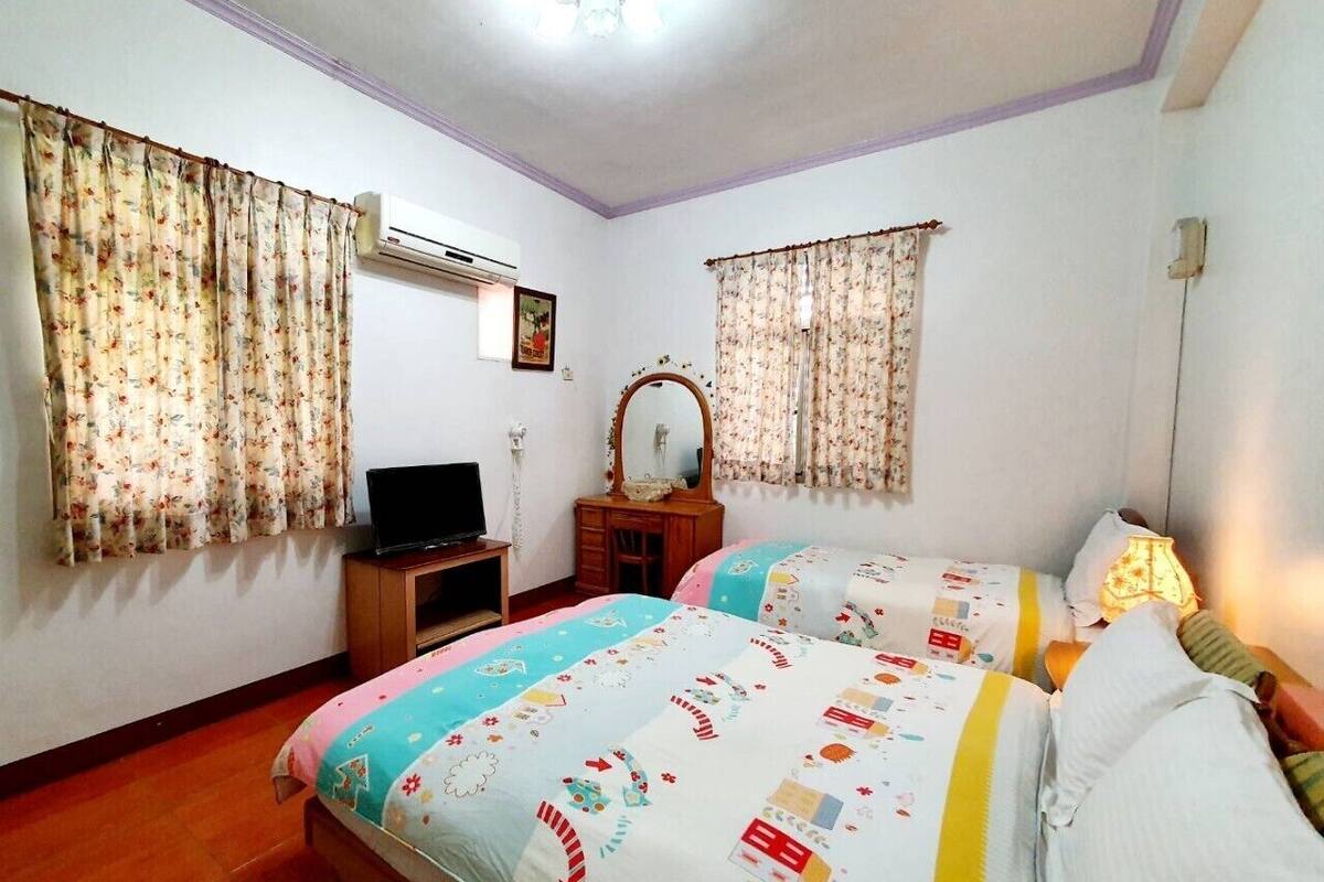 A bedroom with two beds, a dresser, a TV, and an air conditioning unit.