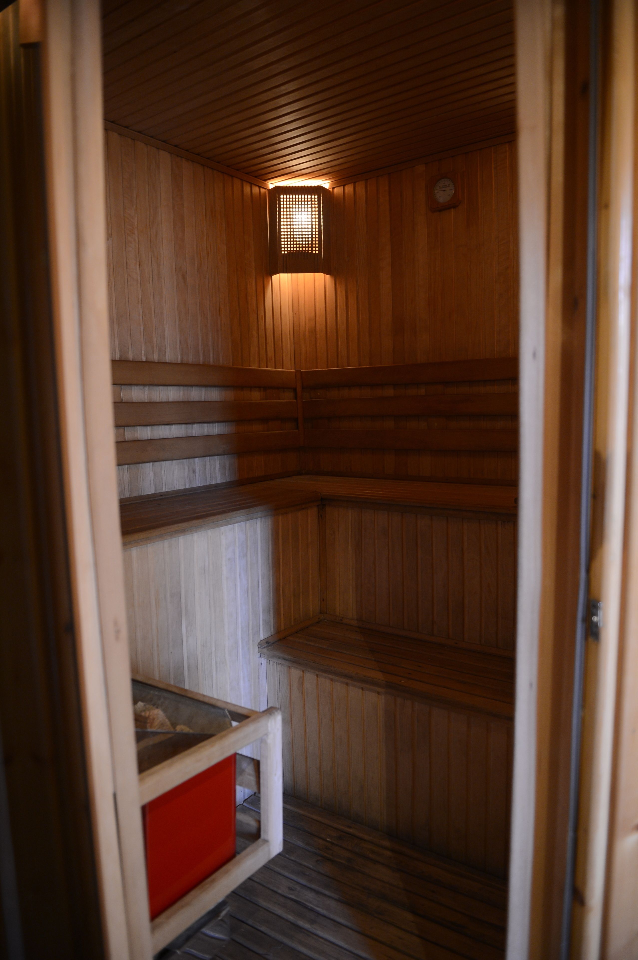 Una sauna con paredes de madera y techo inclinado, que incluye un ventanal pequeño y un caja roja para guardar objetos.