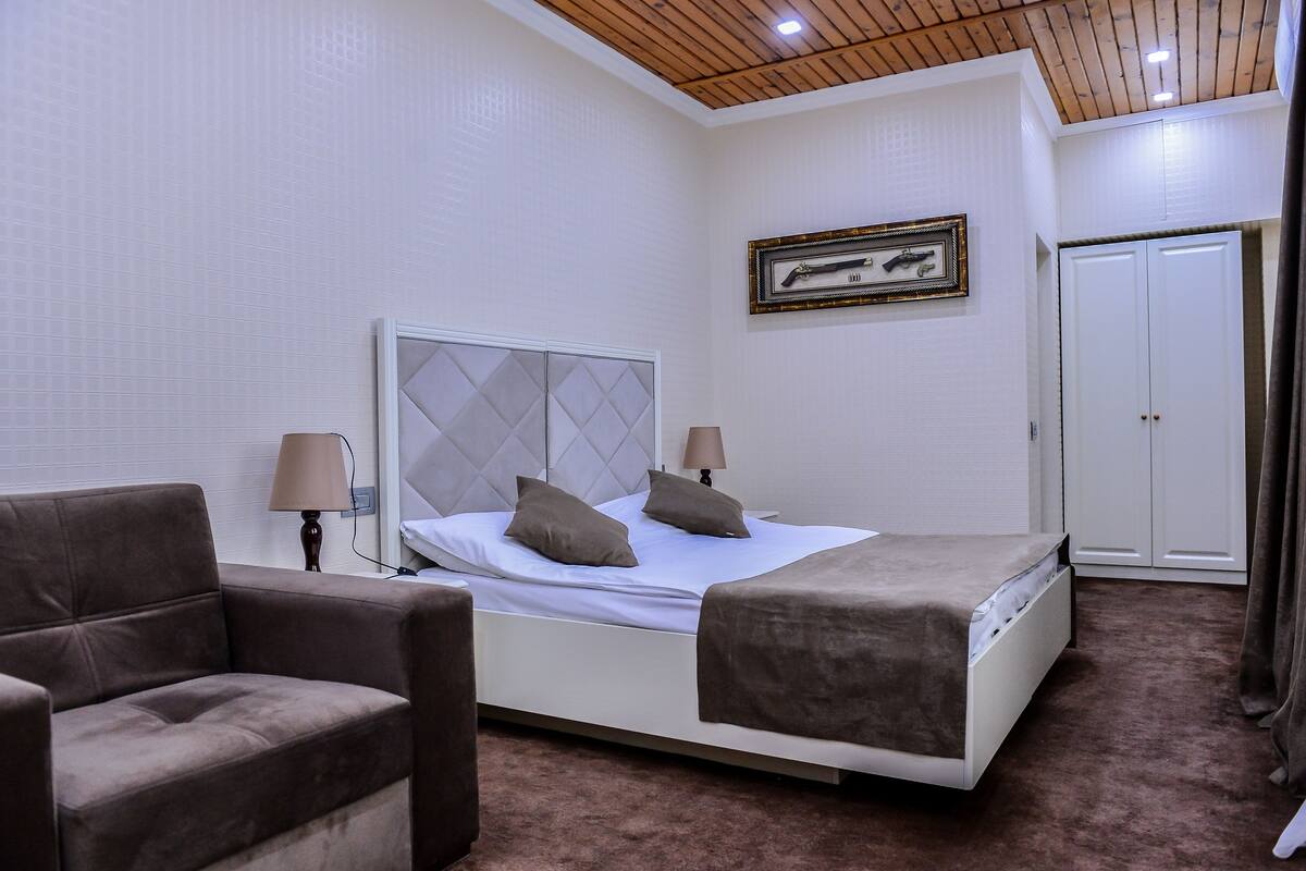 A bedroom with a bed, two bedside lamps, a framed picture on the wall, and a wardrobe.