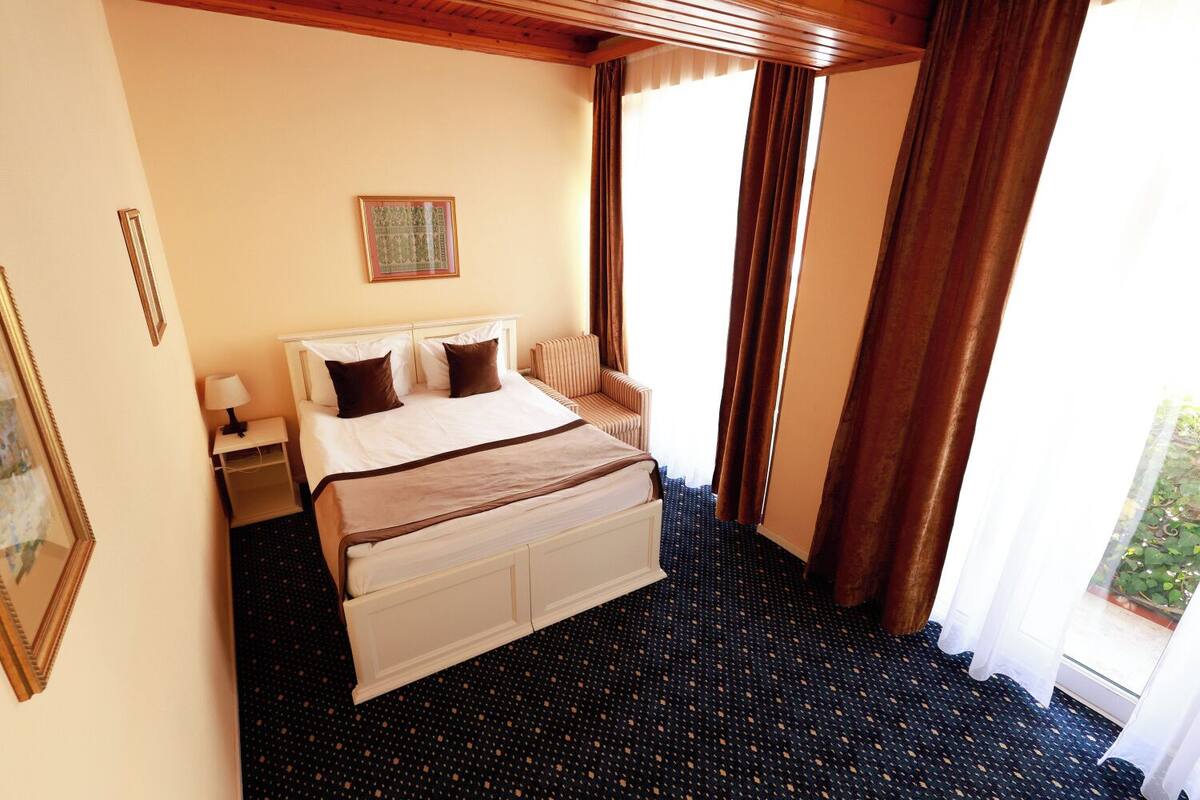 A hotel room with a large bed, a nightstand, a chair, and a window with curtains.