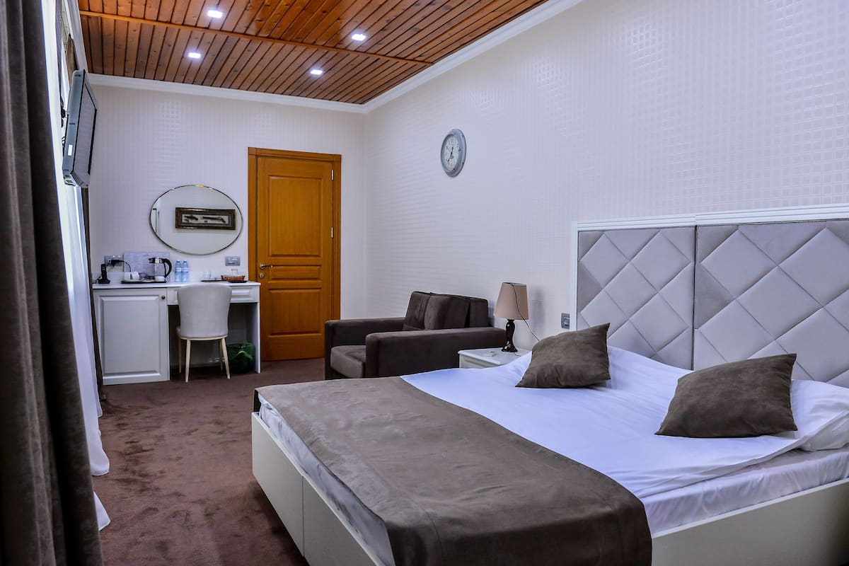 A hotel room with a bed, a desk, a chair, and a clock on the wall.