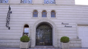 L’entrée d’un hôtel, avec un portail en fer forgé, une enseigne indiquant le restaurant Panorama, et deux plantes en pot.
