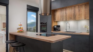 A modern kitchen with a central island, dark cabinetry, and a view of the outdoors. - Villa Marulovo (Okrug)