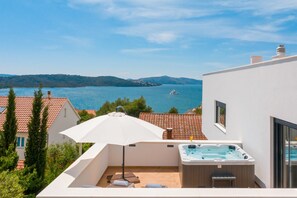 A rooftop terrace with a hot tub, outdoor seating, and a view of a lake and mountains.