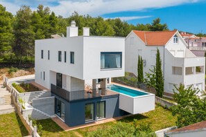 A modern two-story house with a swimming pool, a balcony, and a well-maintained garden.