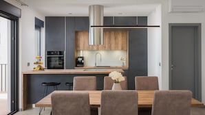 A modern kitchen with a central island, stainless steel appliances, and a dining area with a wooden table and chairs. - Villa Marulovo (Okrug)