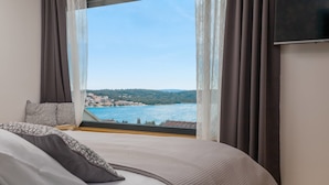 A bedroom with a large window offering a view of a coastal town and sea. - Villa Marulovo (Okrug)