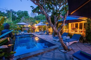 A pool area with lounge chairs and umbrellas, surrounded by trees and plants. - 221 Garden cottages (Lembongan Island)