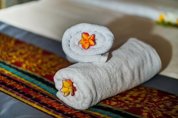 Two rolled towels with floral decorations on a bed with a colorful, patterned bedspread. - 221 Garden cottages (Lembongan Island)