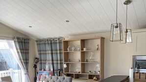 Een moderne keuken met houten kastjes, een zithoek met een grijze bank en een balkon met gordijnen.