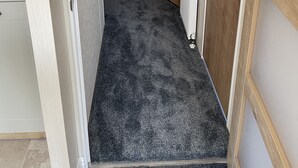 Een smalle gang met een vloerbedekking, houten deuren en een witte radiator.