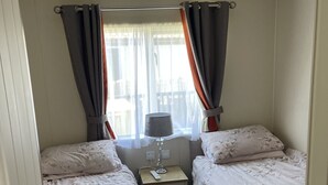 Een slaapkamer met twee bedden, een nachtkastje, een lamp en een raam met gordijnen.