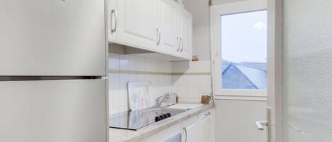 A compact kitchen with white cabinets, a built-in oven, and a window offering a view of the sky.