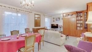 A dining area with a table set for four, a sofa, and a television in the background. - Le Hoche by Interhome (Dinard)