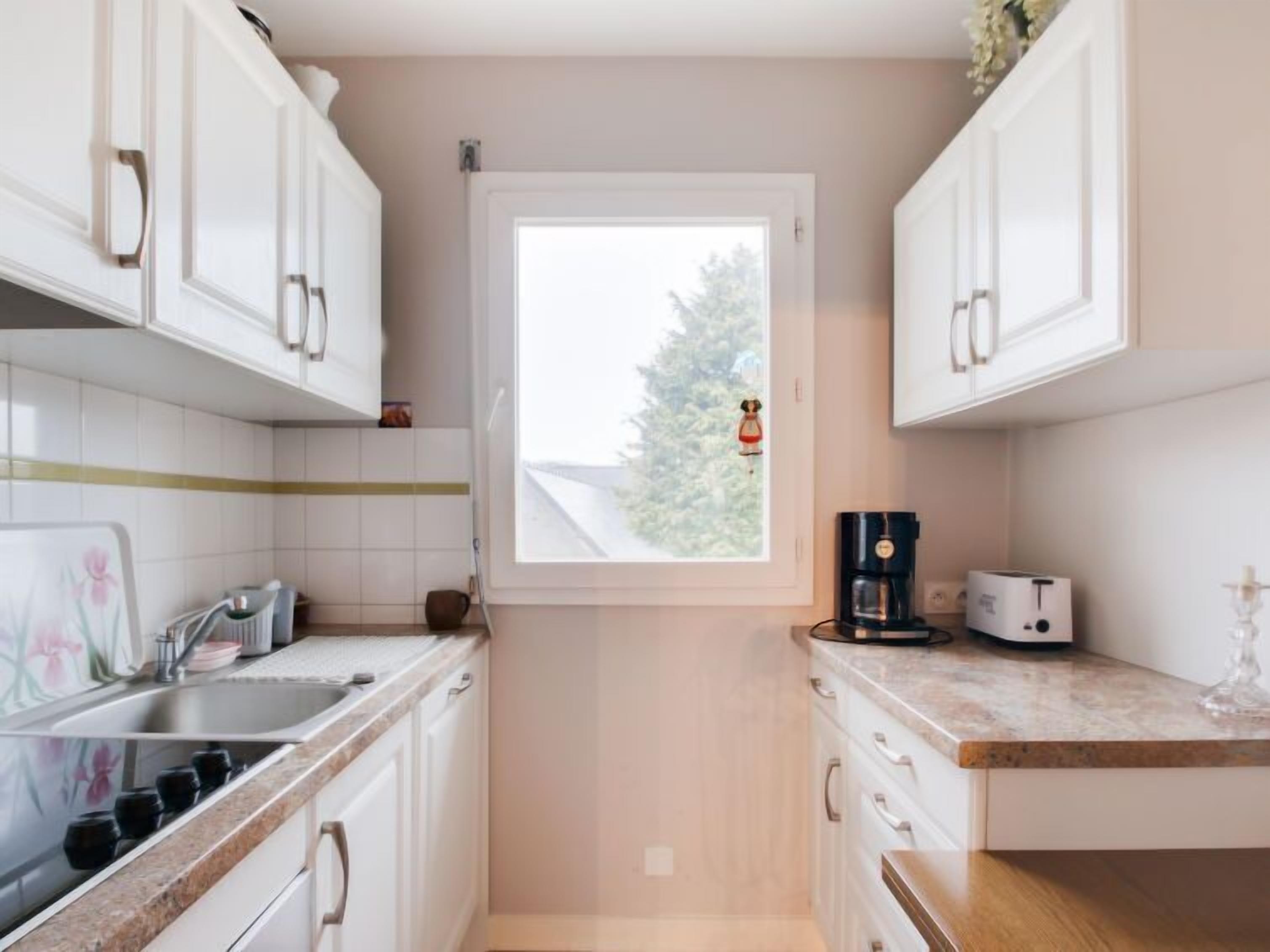 A compact kitchen with white cabinets, a window with a view of trees, a coffee maker, and a toaster on the countertop.
