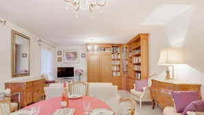 A dining area with a pink tablecloth, wooden cabinets, and a chandelier. - Le Hoche by Interhome (Dinard)