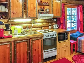 A cabin-style kitchen with wooden cabinets, a stove, and a sink. - Mäntyniemi by Interhome (Rääkkylä)