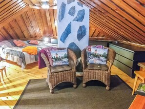 Una habitación acogedora con techo inclinado, una cama con colcha estampada, dos sillones de mimbre con cojines y una pared decorada con una gran formación rocosa.