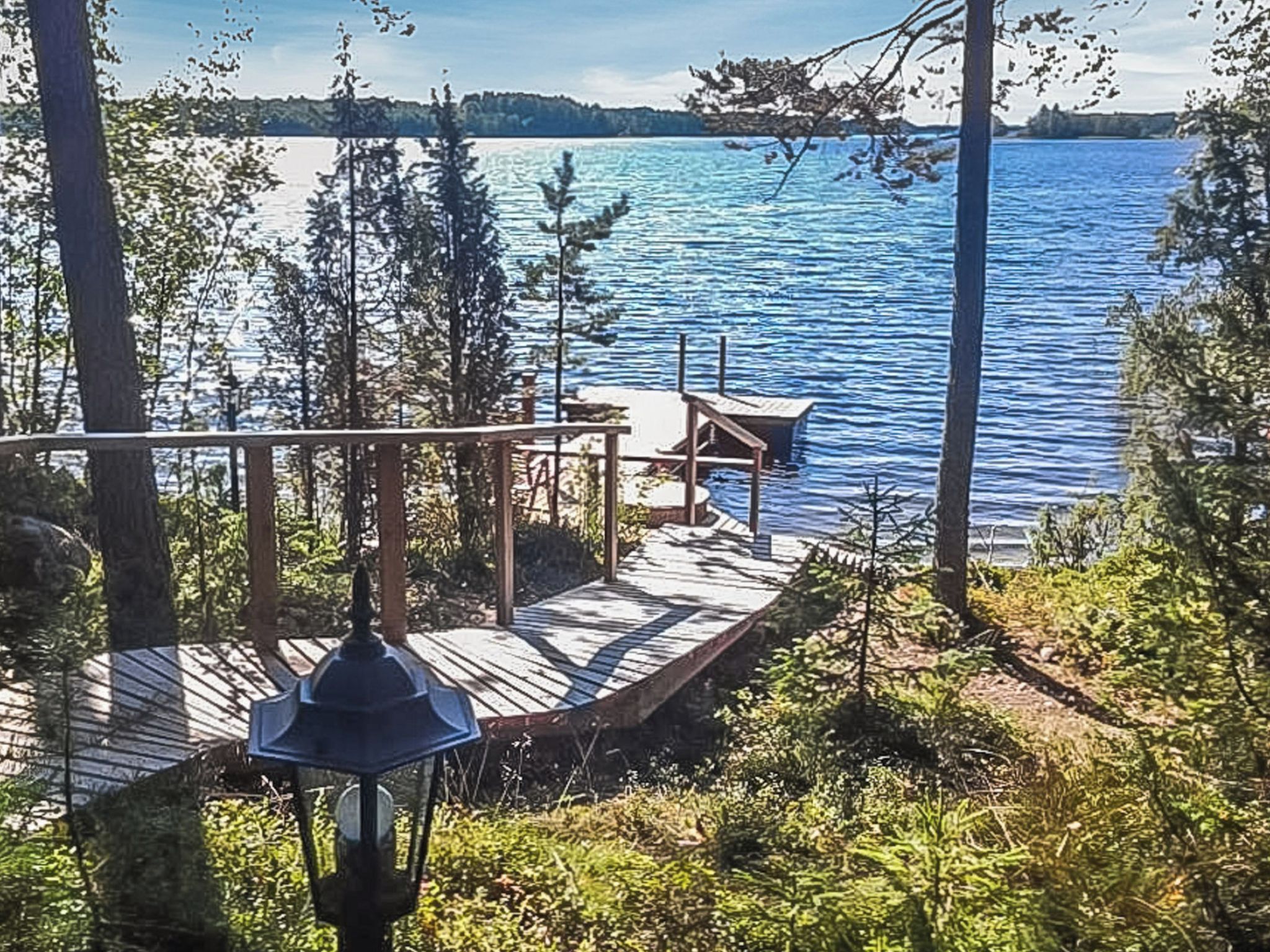 Eine Holzterrasse mit Bank und Tisch mit Blick auf einen ruhigen See, umgeben von Bäumen.