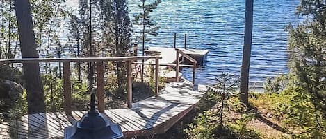 Eine Holzterrasse mit Bank und Tisch mit Blick auf einen ruhigen See, umgeben von Bäumen.
