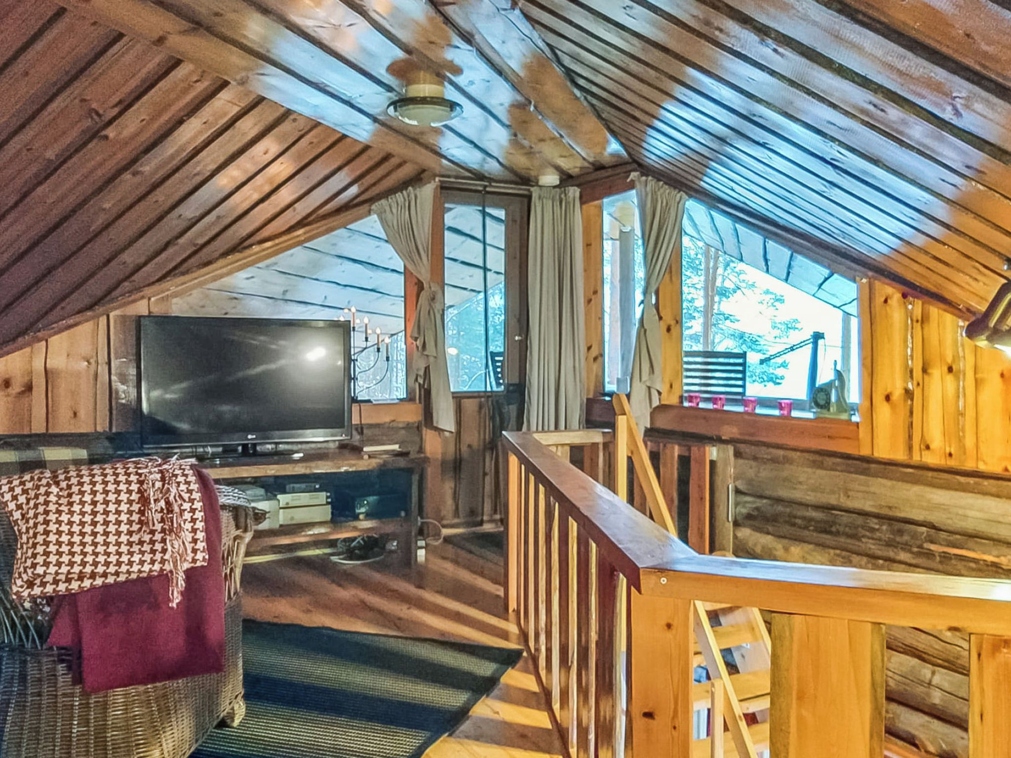 A cozy attic room with a television, a cushioned chair, and a wooden railing.