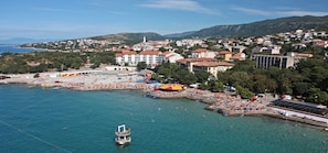 Luftaufnahme einer Küstenstadt mit Strand, Gebäuden und einem Bergpanorama im Hintergrund.