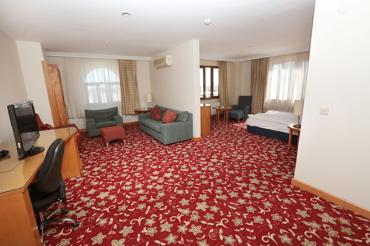 Une chambre d’hôtel avec un tapis à motifs floraux rouges, un canapé, un lit, un bureau avec un ordinateur et une chaise.