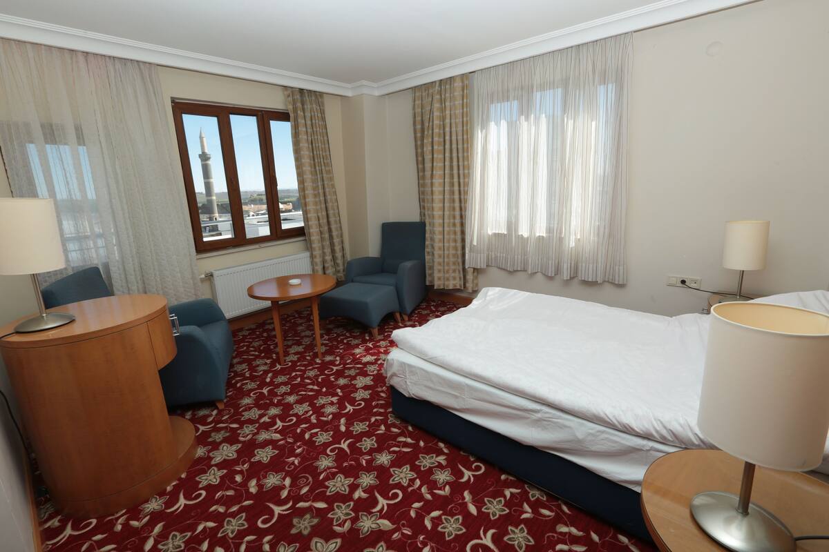 Une chambre d’hôtel avec un lit, deux fauteuils, une petite table et une vue sur une tour par la fenêtre.