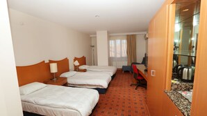 Een hotelkamer met drie bedden, een bureau, een stoel, een televisie en een kitchenette.