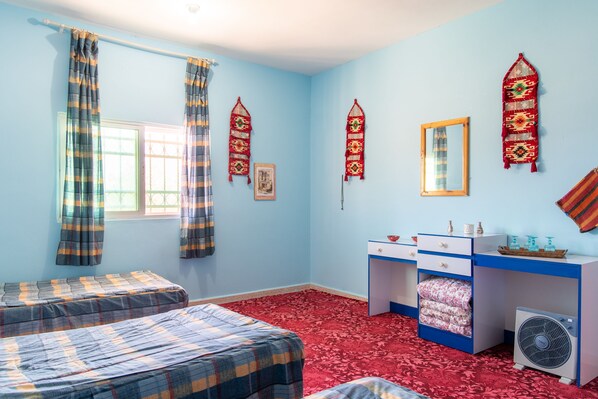 Una habitación con dos camas, un escritorio, una silla, un ventanal con cortinas, un espejo montado en la pared y un radiador.