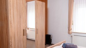 Hotellihuone, jossa on puinen vaatekaappi, valkoisilla lakanoilla varustettu sänky ja patteri.