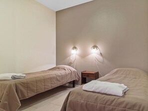 A hotel room with two single beds, a nightstand, and wall-mounted reading lights.