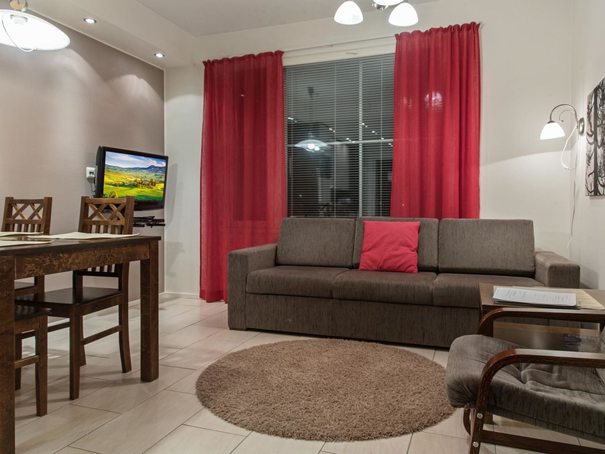 Una sala de estar con sofá, mesa de comedor, sillas, televisor y cortinas rojas.