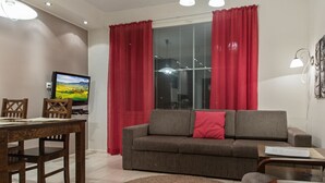 A living room with a sofa, a dining table, chairs, a TV, and red curtains.