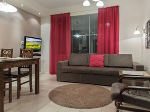 A living room with a sofa, a TV, a dining table with chairs, and a window with curtains.
