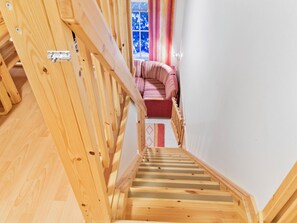 A wooden staircase leading to a room with a window and a striped sofa.