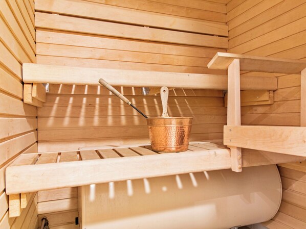 A sauna with wooden benches and a copper bucket.