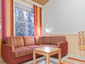 A living room with a sofa, a coffee table, a window with curtains, and a wall-mounted light fixture.