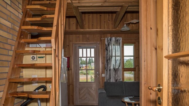 A wooden staircase leading to a living area with a sofa, a small table, and a door with a window.