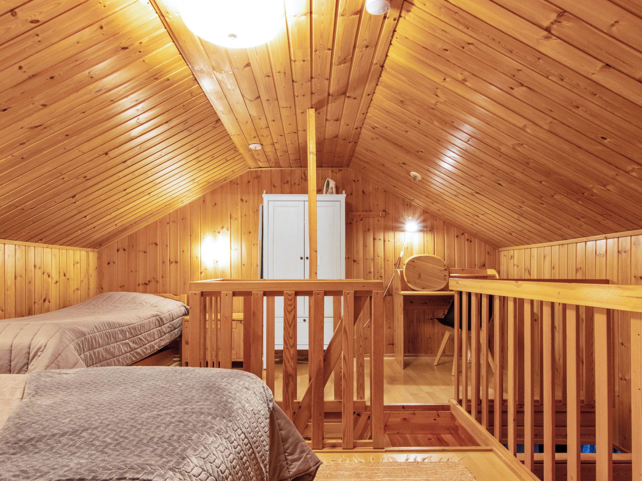 Puinen ullakkohuone, jossa on kaksi sänkyä, puinen portaikko ja valkoinen vaatekaappi.