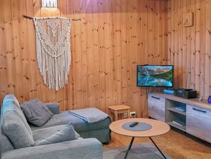 Une pièce chaleureuse avec un mur en bois, un canapé gris, une télévision et une petite table.
