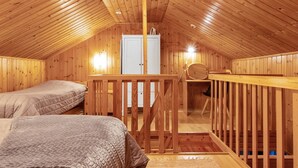 A wooden attic bedroom with two beds, a desk, and a wardrobe.