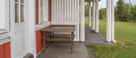 A wooden bench on a porch with a white railing and a red wall.