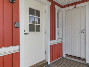 A white door with a small window, a porch with a wooden floor, and a red siding exterior.