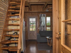A wooden interior with a staircase, a door leading to a room with a gray sofa, and a window with a view.