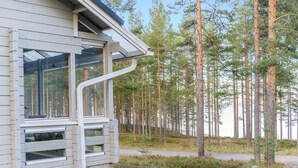 Une maison moderne dotée de grandes fenêtres et d’un toit en pente, entourée d’une forêt.