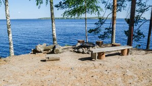 Un terrain de camping au bord du lac, équipé d’un banc, d’un foyer et de bûches.